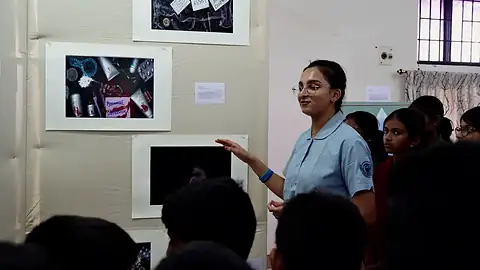 A student gestures towards framed photographs on a display wall as younger students listen