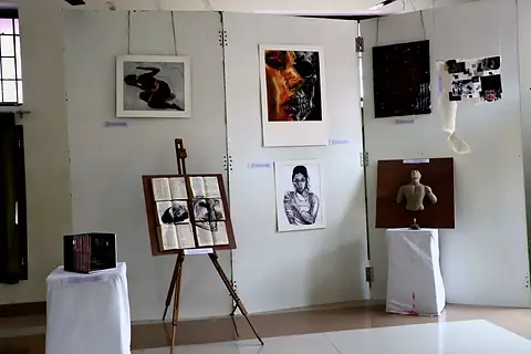 A display wall of drawings and paintings, with an easel holding a drawing on book pages, a relief torso and a boxed model on plinths