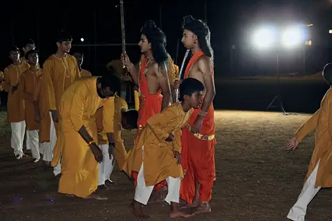 Students in saffron dancing on the field at night under floodlights