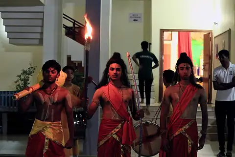 Students in costume as Rama, Lakshmana and Hanuman leaving a building by torchlight