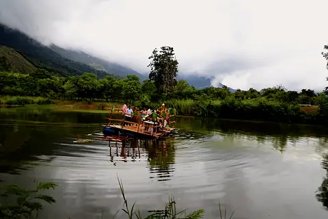 A small raft far out on a still lake, forested hills and cloud behind it
