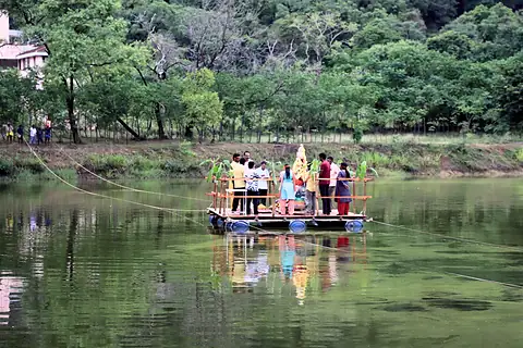 A raft with the murti and a group aboard, reflected in green water