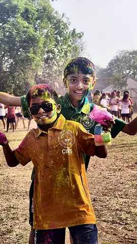 A boy in an orange CIRS shirt covered in colour, grinning, a friend behind him
