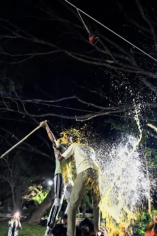 A student at the top of a human pyramid strikes the pot, and its contents burst out in the floodlight
