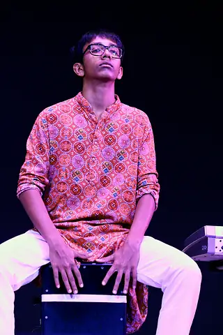 A student playing a cajon on stage under violet light