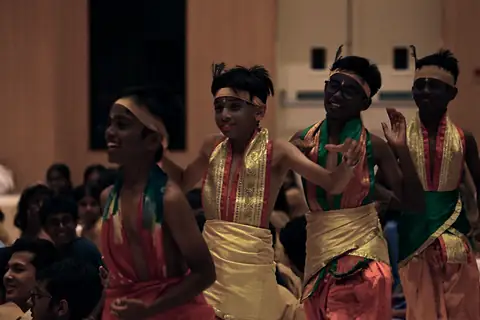 Students in red and gold costume and headbands dancing close to the audience