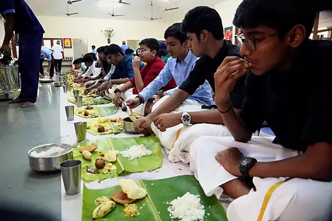 A student in a white mundu eating rice from a banana leaf