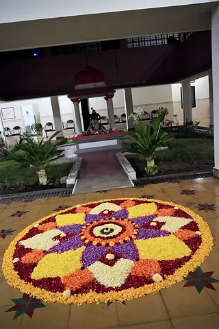 A circular flower pookalam in yellow, orange and purple laid on a courtyard floor