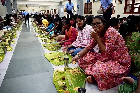 Girls seated in a row on the floor with banana leaves before them, the row running into the distance