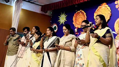 Teachers in cream and gold kasavu singing together on stage