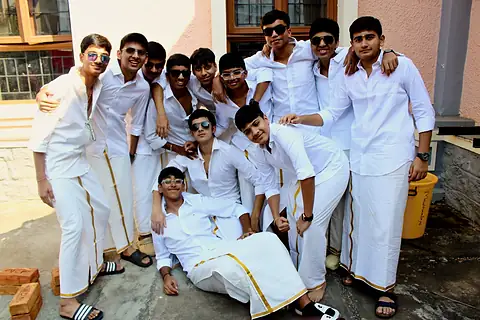 A group of boys in white shirts and veshti posing together in the sun