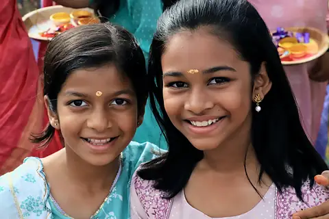 Two girls with tilak on their foreheads smiling at the camera
