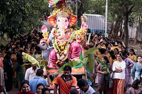A decorated Ganesh murti carried through a crowd of students and staff