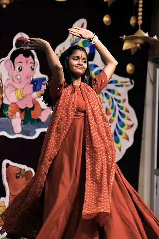 A girl in a red dress dancing with her arms raised in front of a festival backdrop