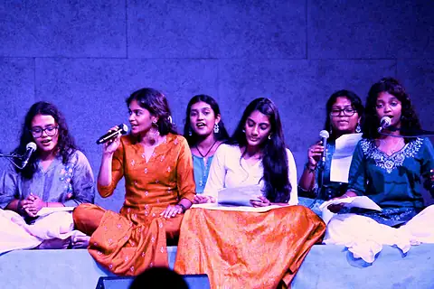 Students singing into microphones on a stage lit in blue