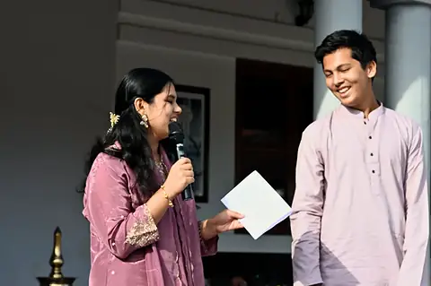 A girl speaking into a microphone beside a boy in a kurta