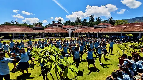 Students in blue and grey standing in formation on a lawn in front of the school buildings