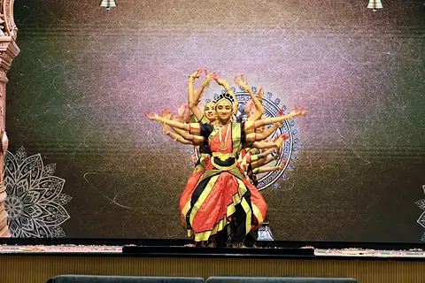A dancer in red and gold at the centre of a many-armed tableau