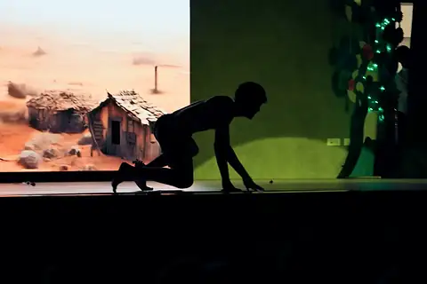 A figure crawling in silhouette before a projected desert and a ruined hut