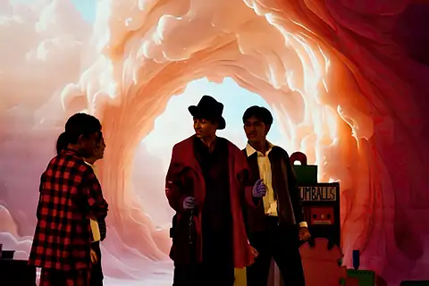 Actors before a swirling pink tunnel projected behind them