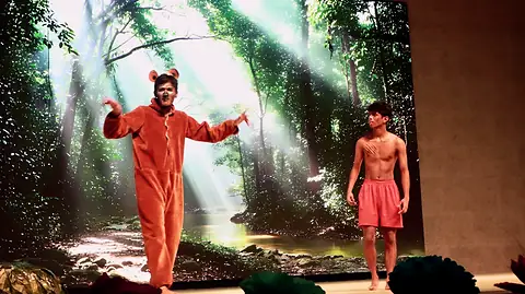 The actor in the bear costume and a boy in a forest clearing lit by shafts of light
