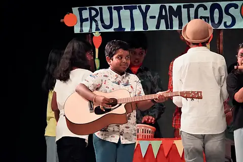 A boy playing a guitar at a stall beneath a hand-painted sign