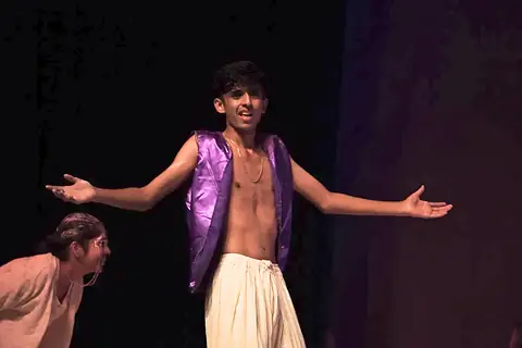An actor in a purple waistcoat with arms spread