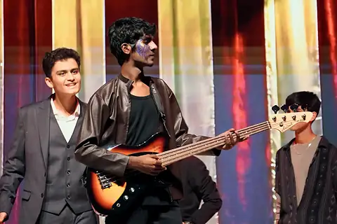 An actor with a bass guitar between two others before striped curtains