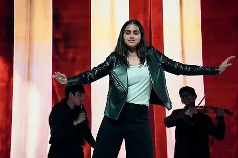 A performer in a leather jacket, arms spread, before striped curtains