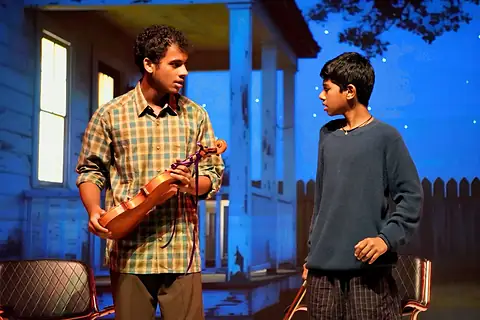 An actor holding a violin and a boy on a porch set at night