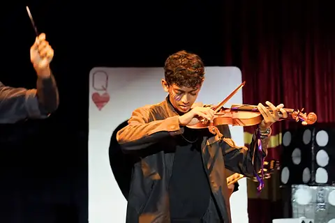 An actor playing a violin before a giant playing card