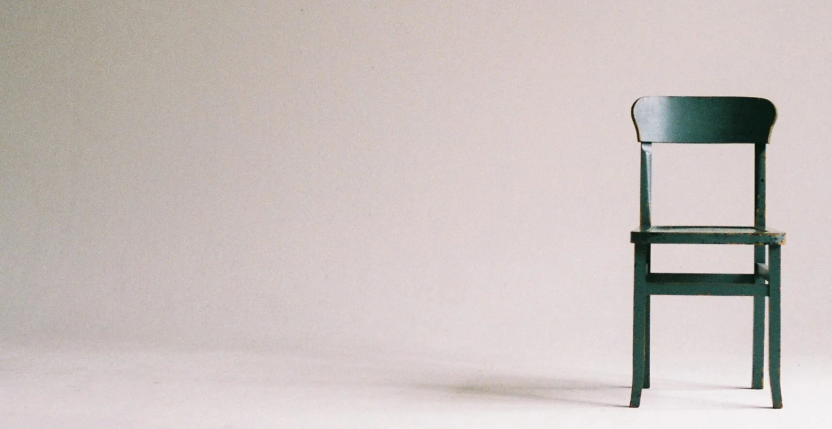 A plain wooden chair alone against a bare grey wall