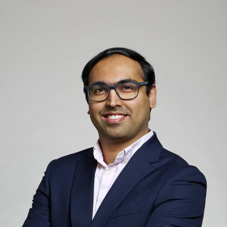 Hari Om Jani wearing glasses and a navy jacket against a plain background.
