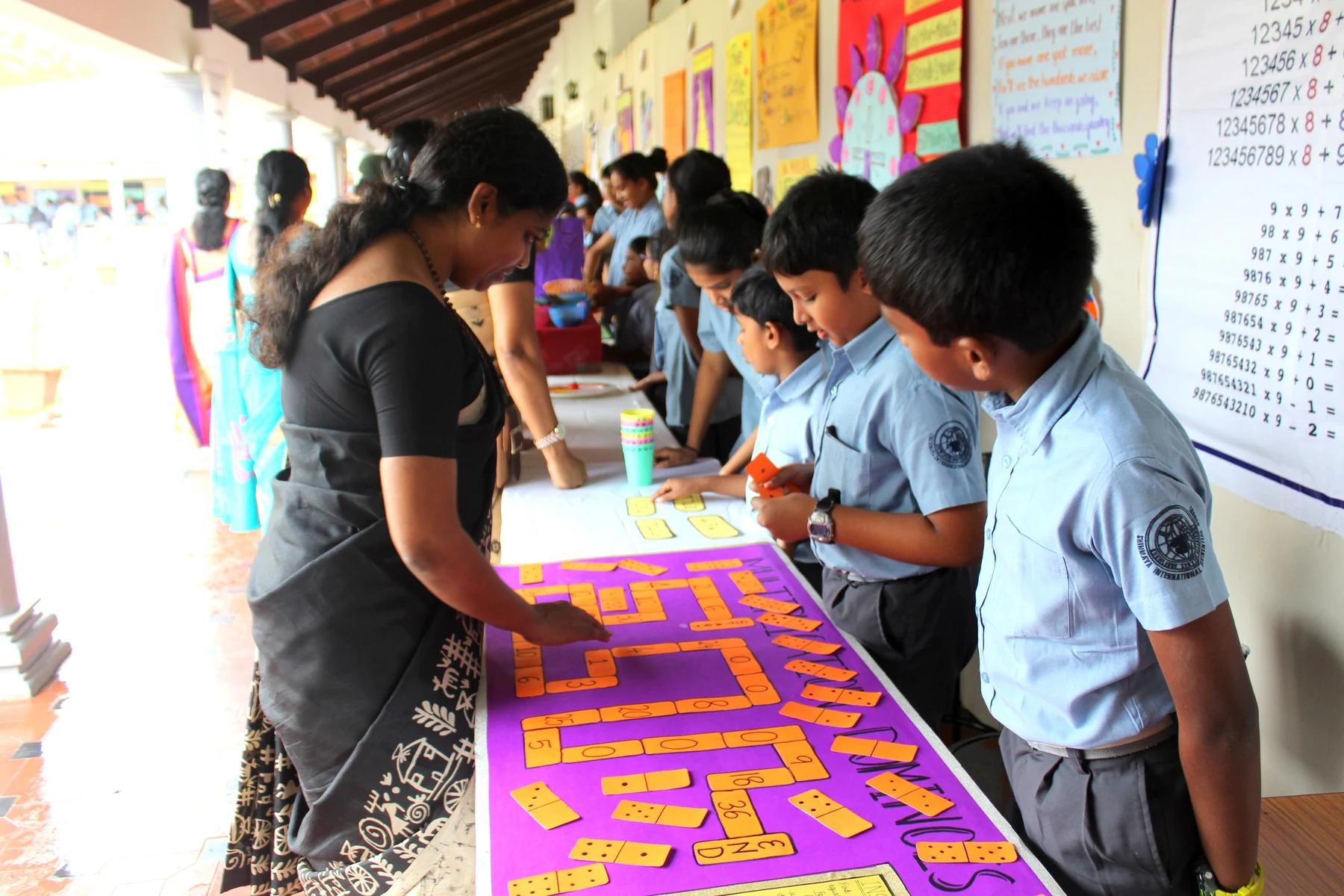 A teacher and students at a long table, working on a purple banner with yellow lettering
