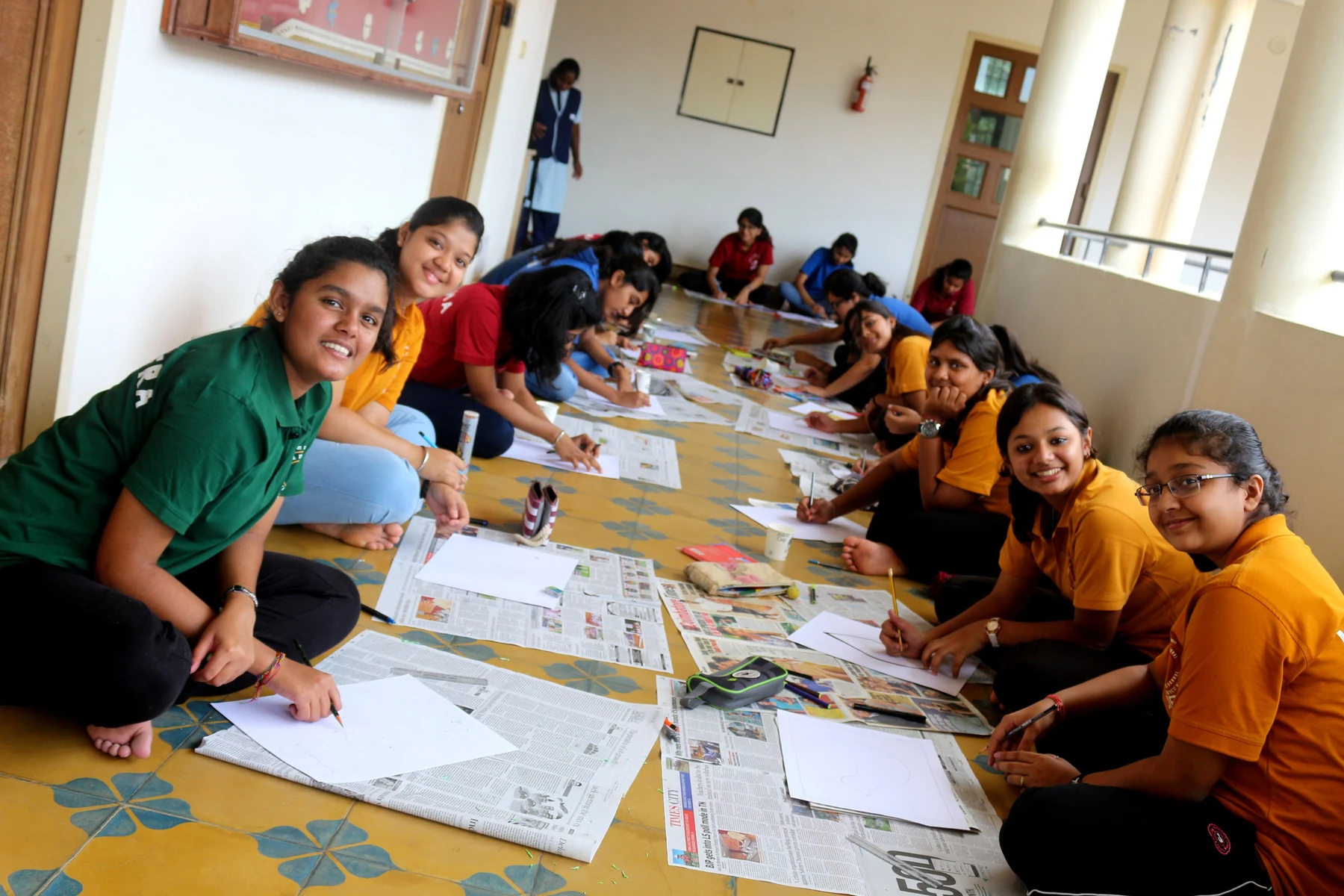 Students seated on the floor around sheets of paper, painting and drawing