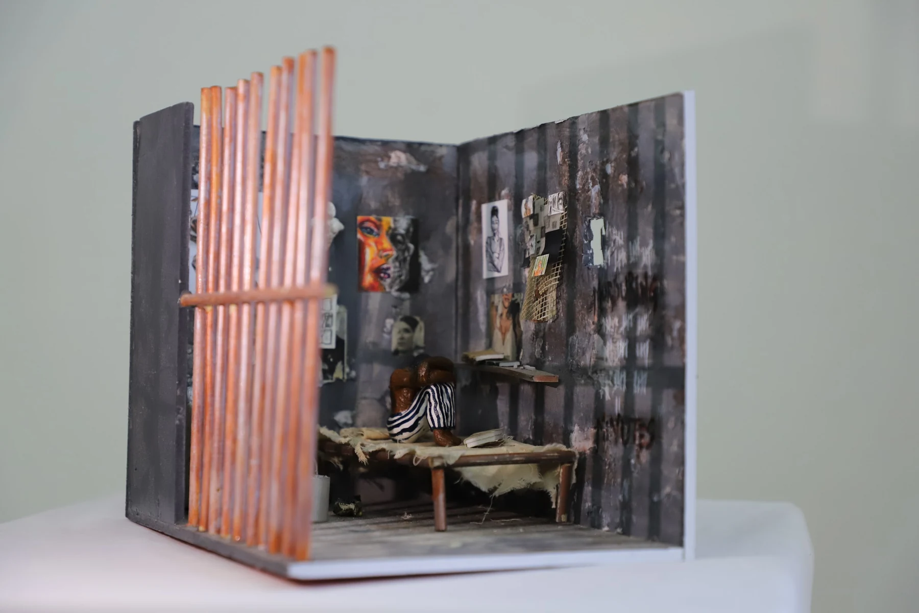 A model room seen through wooden bars, its walls covered in small pictures