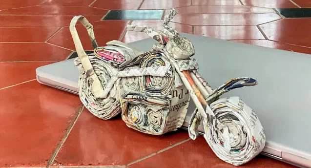 Photograph of a motorcycle made of rolled newspaper, on a red floor