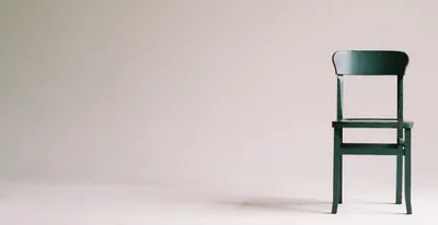 A plain wooden chair alone against a bare grey wall