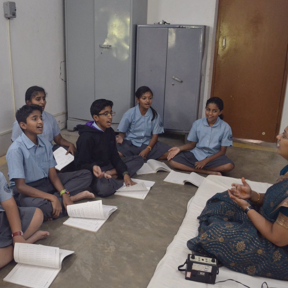 A small group of students seated on the floor with their teacher, books open in front of them