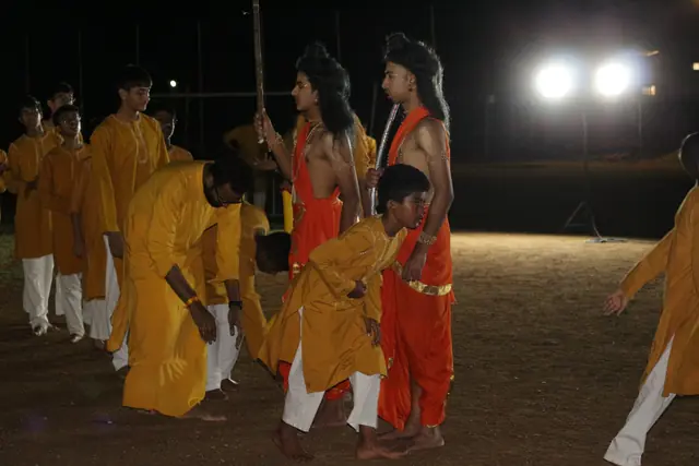 Students in saffron dancing on the field at night under floodlights