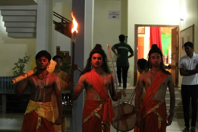 Students in costume as Rama, Lakshmana and Hanuman leaving a building by torchlight
