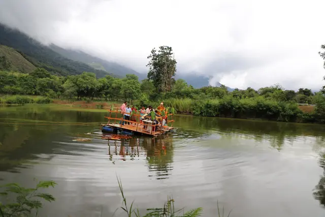 A small raft far out on a still lake, forested hills and cloud behind it