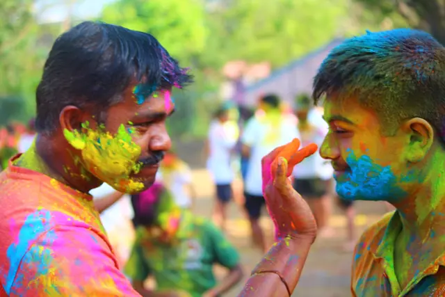 A hand pressing colour onto a student's cheek, both faces already bright with it
