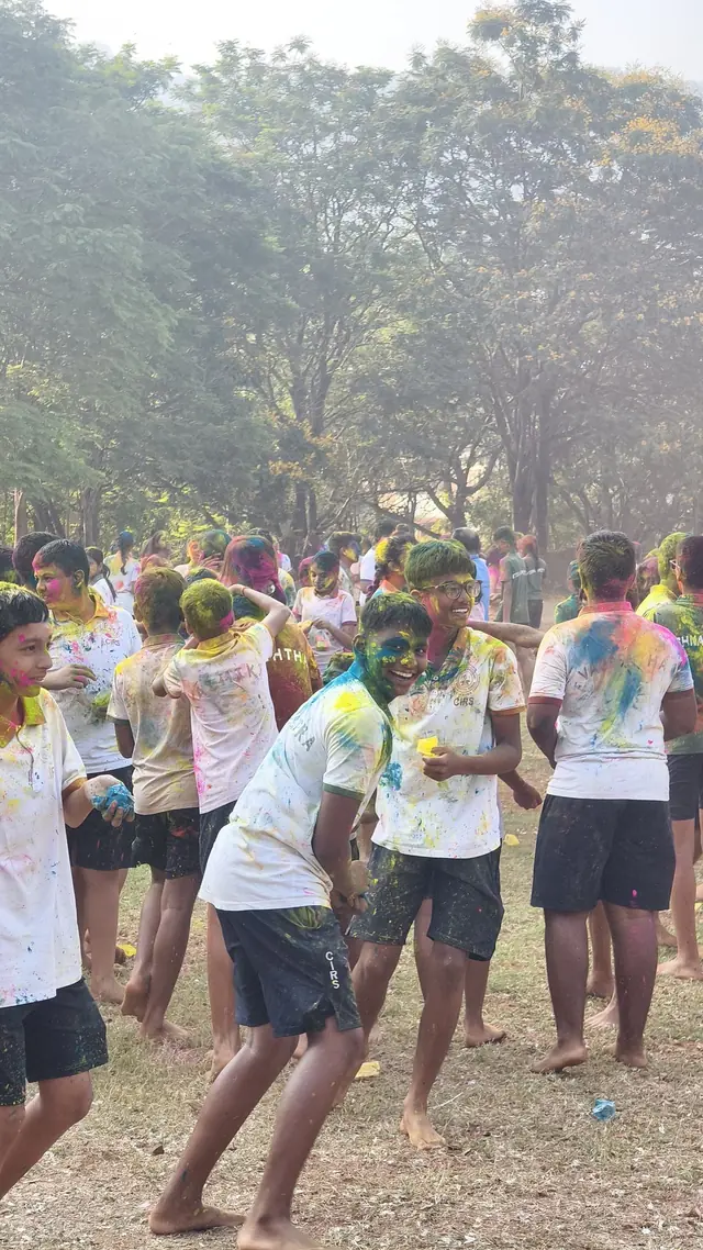 A crowd of students in colour-streaked clothes on the field under trees