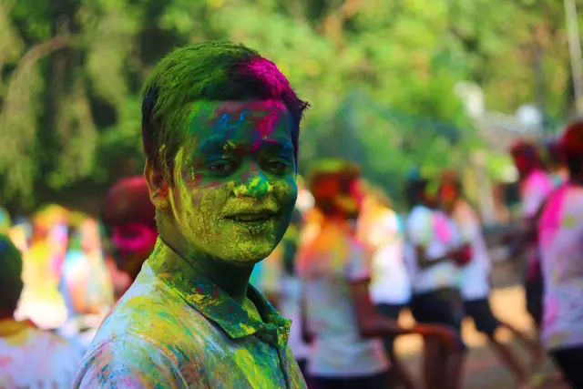 A student looking into the camera, face coated in green and pink colour