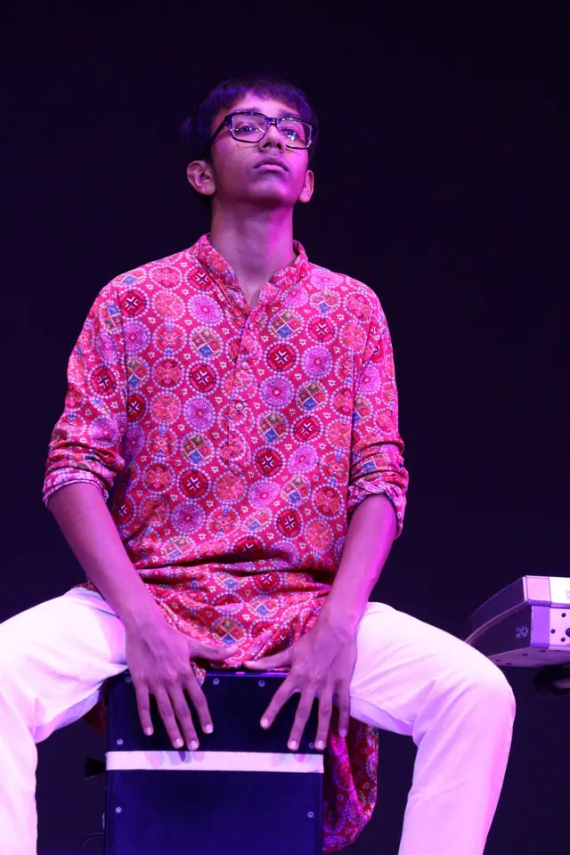 A student playing a cajon on stage under violet light