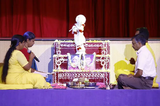 Teachers seated on either side of a flower-decked altar with a white Krishna murti