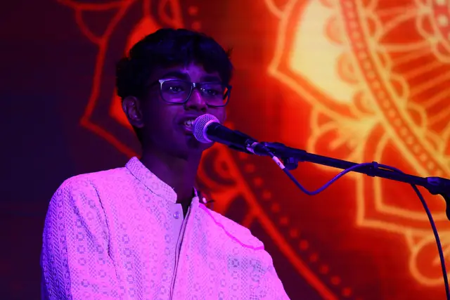 A student singing at a microphone before a red and gold projected mandala