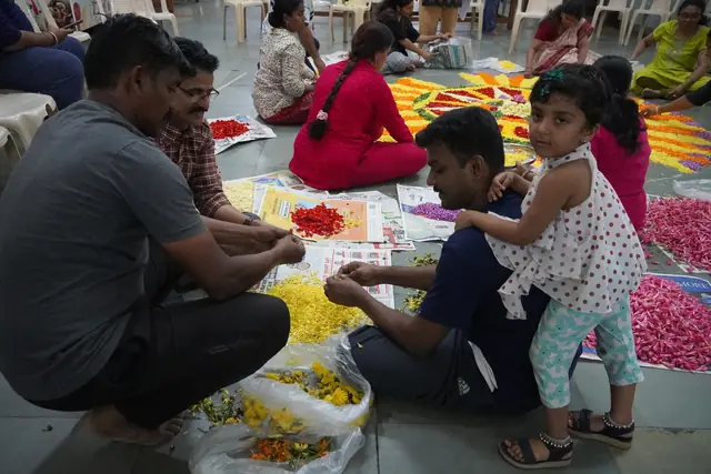 Hands sorting marigold and rose petals on the floor beside a half-laid pookalam
