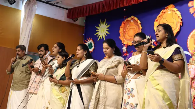 Teachers in cream and gold kasavu singing together on stage